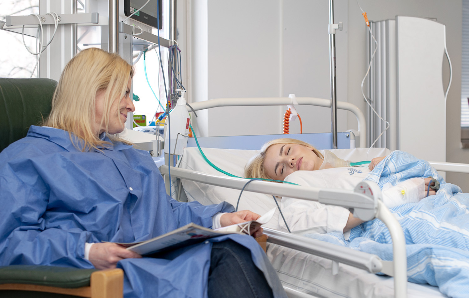 Teenage girl sleeping in her bed in the recovery ward. Her mother is sitting beside the bed.