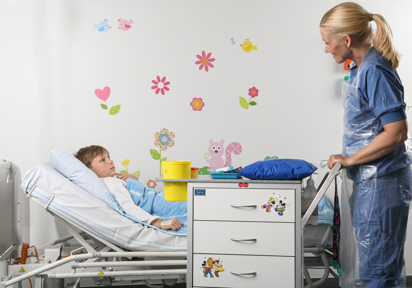 Nurse Lollo in blue clothes pulls a huge trolley carrying boxes across to Frank’s bed.