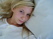 A blond girl in a bed with white sheets