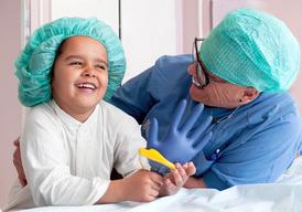 A girl and a nurse sitting beside each other are laughing. The girl has a blue glove in her hand.