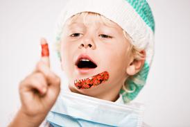 A boy in a green and white scrub cap and a plaster on his chin is pointing up in the air with his finger.