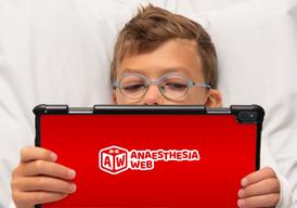 A boy in round blue glasses lying in his bed looking at a red Ipad.