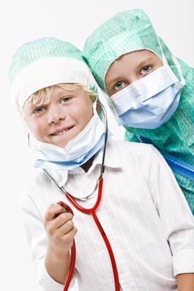 A boy and a girl in scrub caps and face masks looking into the camera. The boy has a red stethoscope around his neck.