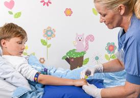 A boy is lying in a hospital bed while a nurse is giving him an injection in his right hand.