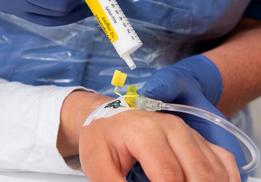 Nurse holding a syringe with medicine in her hand. She is about to give medicine with the syringe in a plastic tube inserted in a blood vessel.